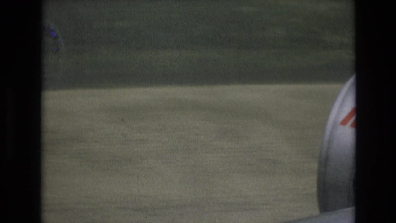 1972 Spain 8mm frame from a passenger window showing the aircraft wing, part of the engine or nacelle, and grassy ground passing below.