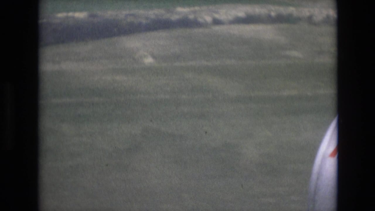 1972 Spain passenger-window view during aircraft descent over green fields, with the window edge and partial aircraft surface at the right.