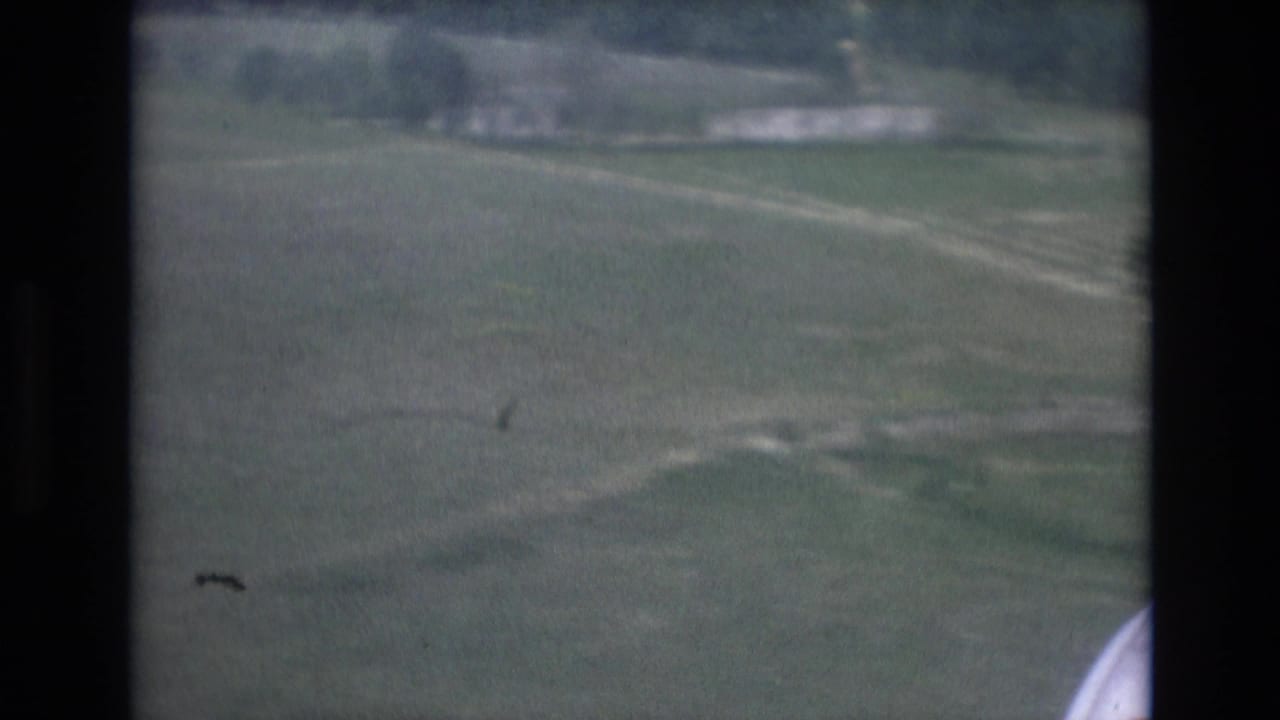 1972 Spain 8mm view from an aircraft window over green fields, dirt tracks, and pale roads during landing approach.