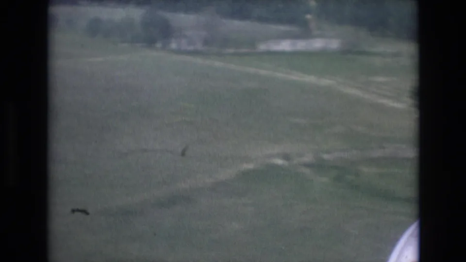1972 Spain 8mm view from an aircraft window over green fields, dirt tracks, and pale roads during landing approach.