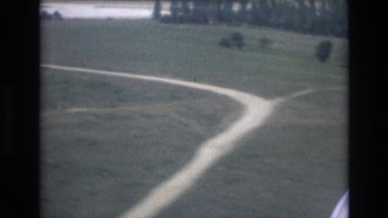 Curving pale road across green land viewed from an aircraft window.