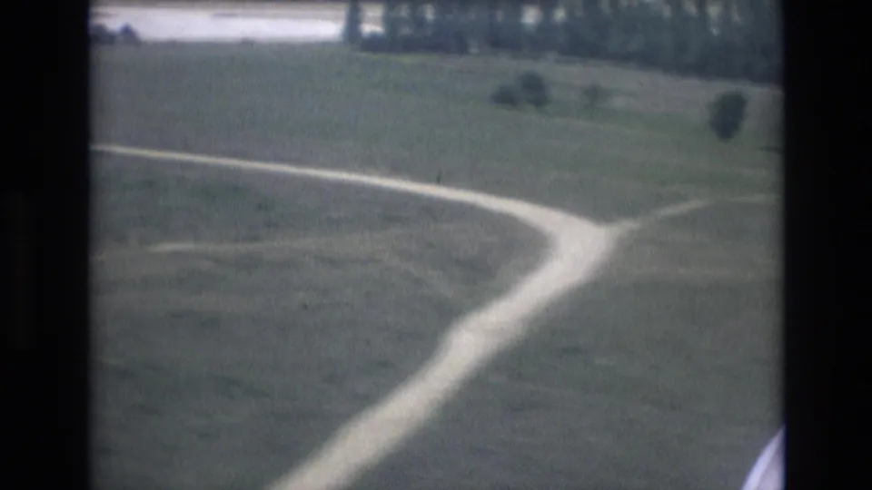 Aircraft-window view over a curving road and open green ground during the 1972 Spain landing sequence.