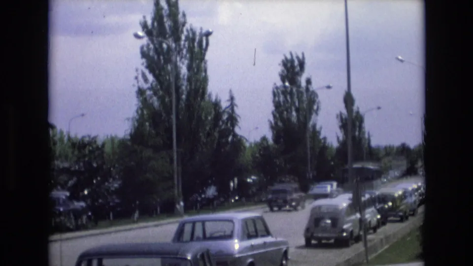 A later frame shows the same Spain road scene with vintage cars, a tree-lined verge, lampposts, and soft handheld 8mm framing.