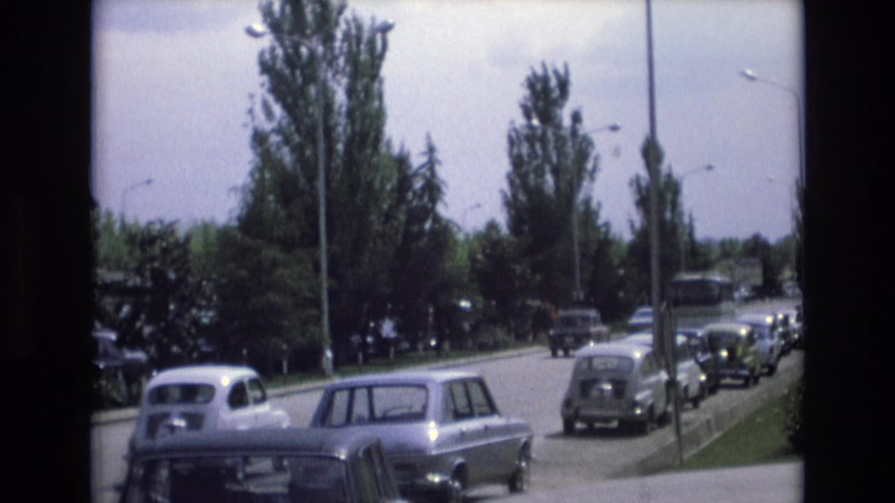 1972 Spain 8mm frame showing classic cars on a tree-lined suburban road with lampposts, curbs, and parked vehicles in view.