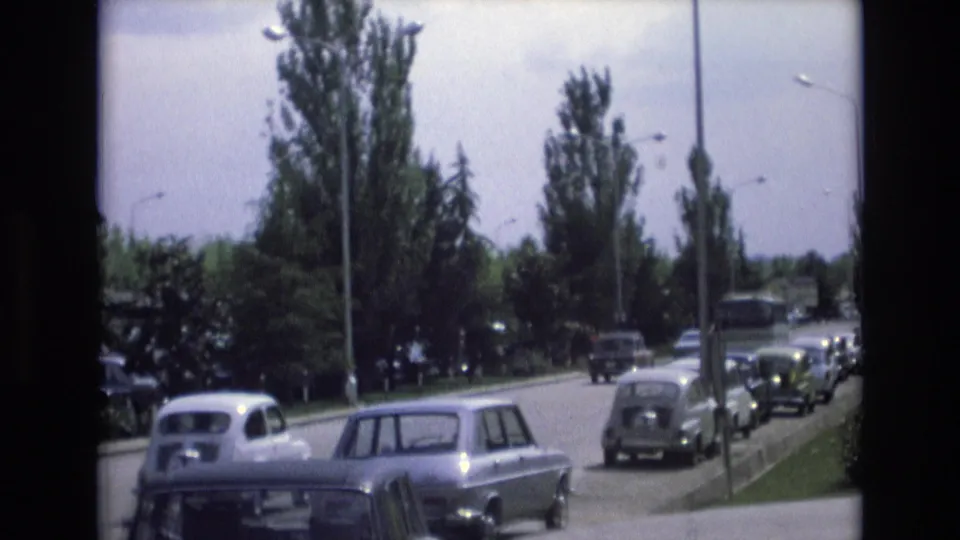 1972 Spain 8mm frame showing classic cars on a tree-lined suburban road with lampposts, curbs, and parked vehicles in view.