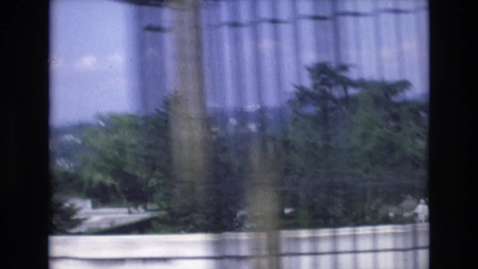 1972 Spain 8mm frame showing a soft, handheld view across a garden terrace with trees, stone edging, distant landscape, and a vertical foreground obstruction.