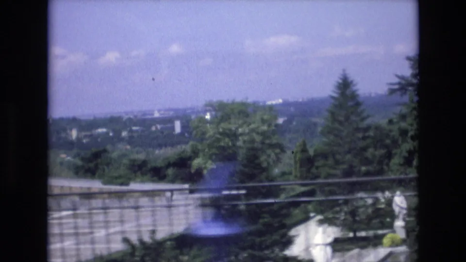 1972 Spain 8mm frame looking from a garden overlook across stone railings, statues, trees, and a distant cityscape under a pale sky.