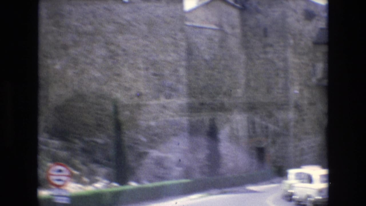 Old stone wall beside a road with a small light-colored car and a roadside sign.