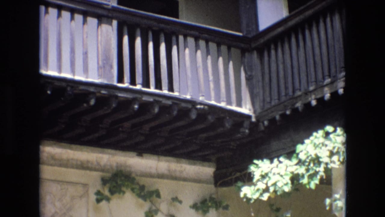 A projecting wooden balcony with vertical slats extends over a carved wall with ivy.