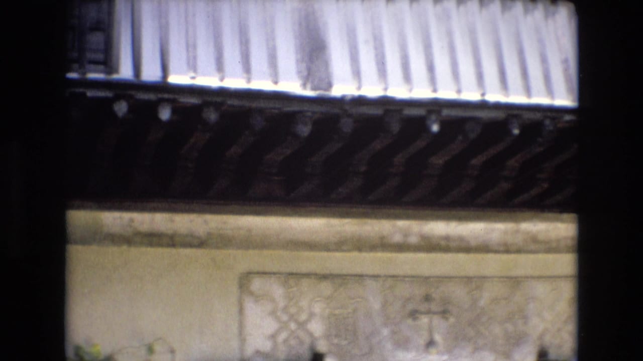 1972 Spain 8mm frame showing part of an ornate courtyard facade with patterned wall panels, a barred window, carved wooden trim, and soft home-movie exposure.