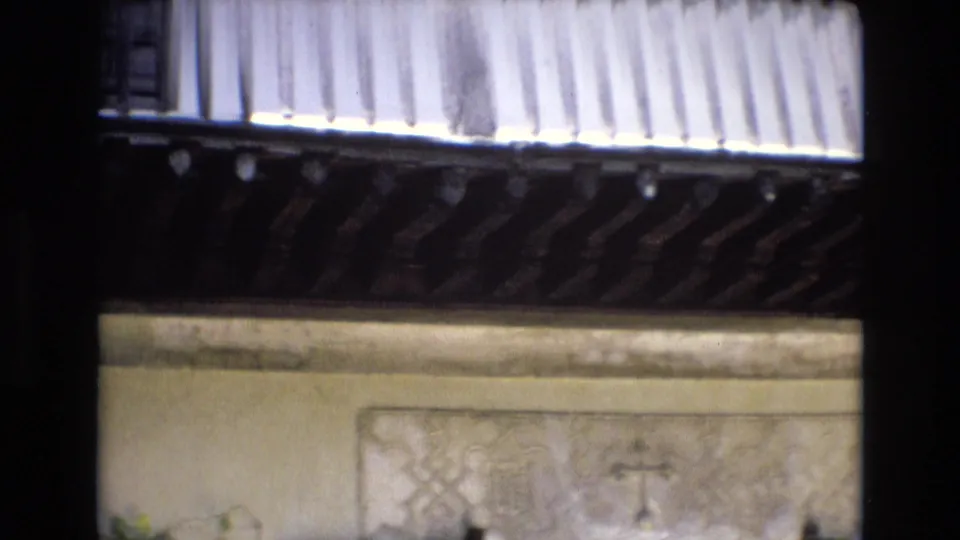 1972 Spain 8mm frame showing part of an ornate courtyard facade with patterned wall panels, a barred window, carved wooden trim, and soft home-movie exposure.