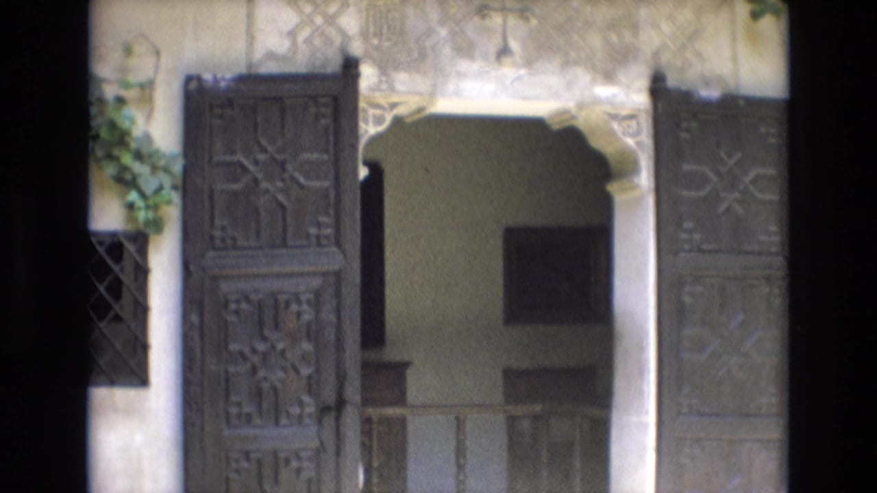 Open carved wooden doors and a stone archway leading into a shaded interior.