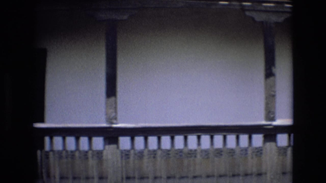 Close 8mm view of a traditional Spanish courtyard balcony with wooden railings, plaster wall, and dark structural shadows.