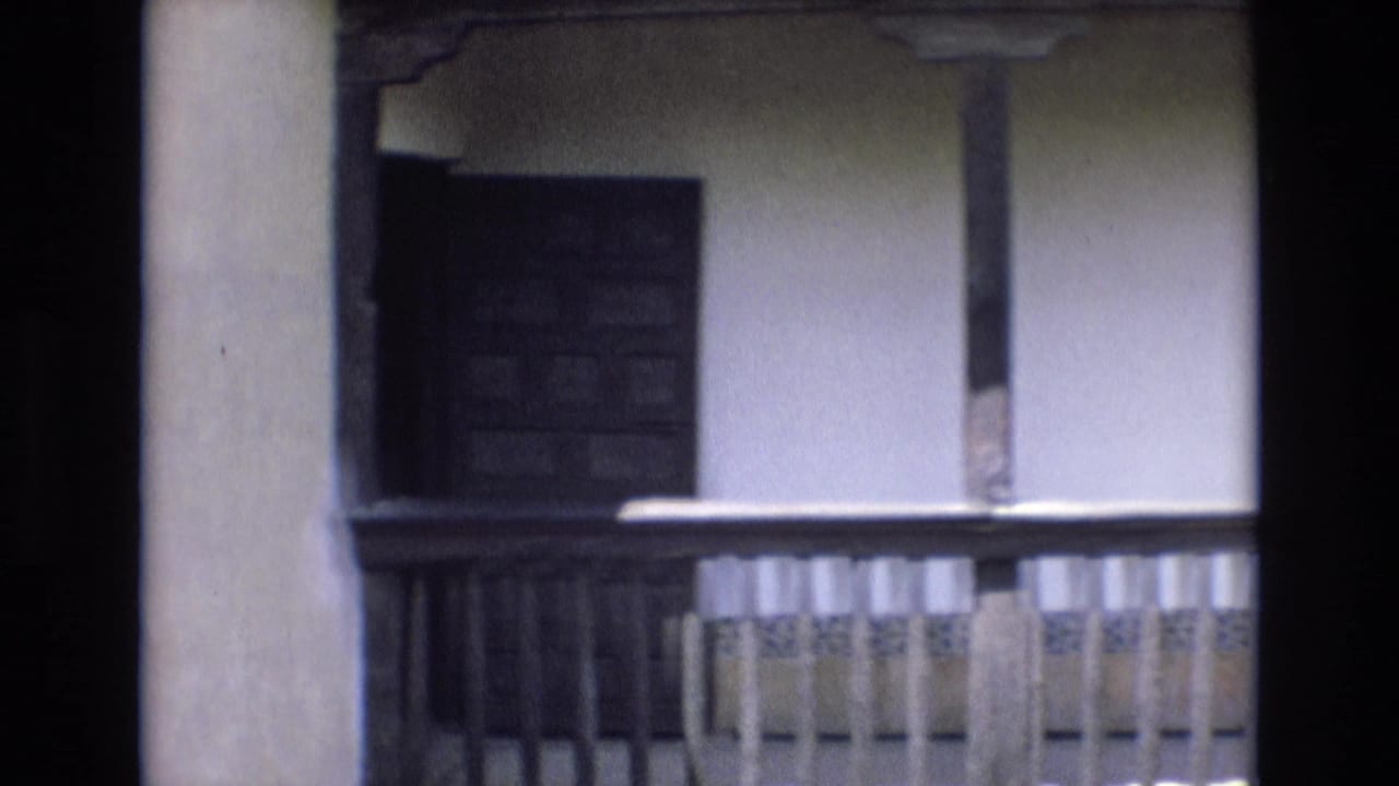 Balcony section with wooden railing, plaster wall, and a dark window opening.