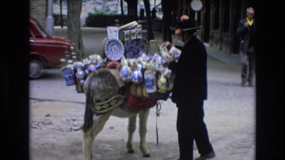 The final frame shows the vendor beside the donkey loaded with blue-and-white goods, with a pedestrian and urban street details in the background.