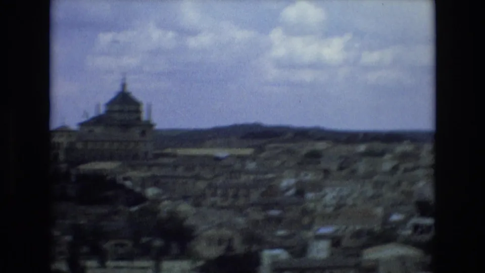 Soft 8mm panorama from Spain in 1972 showing a historic-looking townscape with a prominent domed or towered building under a cloudy sky.