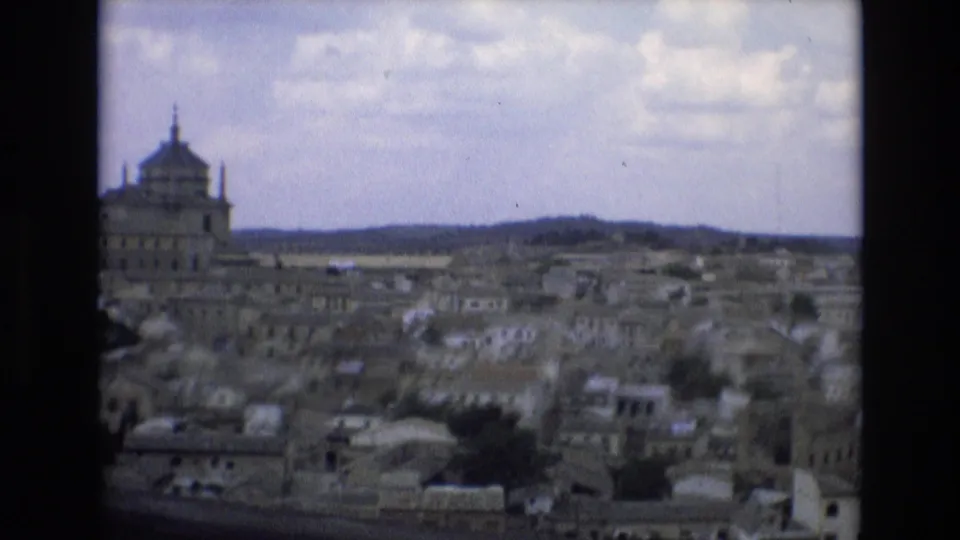 1972 Spain 8mm frame looking across dense historic buildings toward a large domed structure, with hills and cloudy sky in the background.