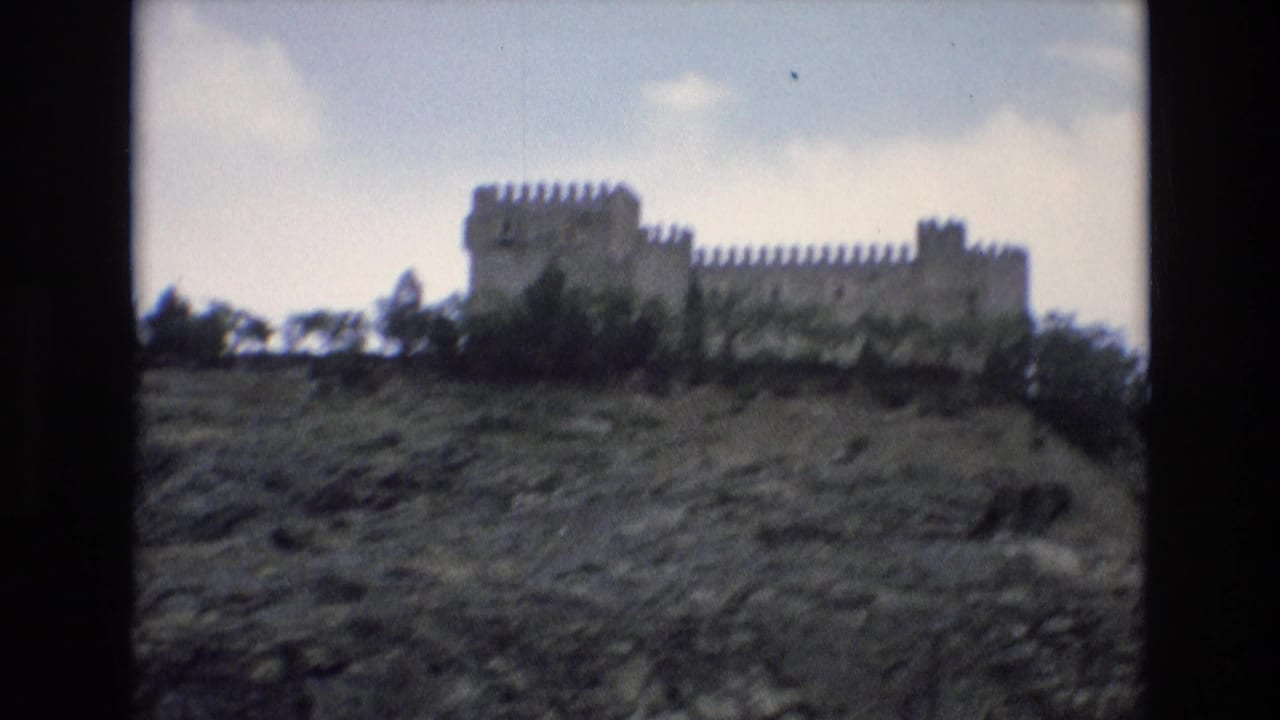 Hilltop castle viewed across sloping rocky ground with trees below the walls.