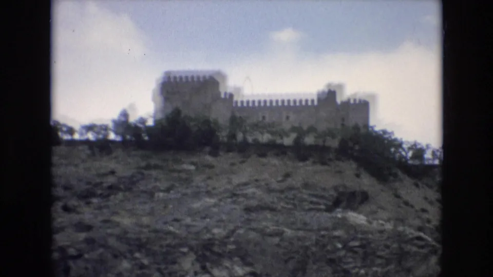 1972 Spain travel-film frame of a crenellated stone building on a hill, filmed from below with soft focus and muted color.