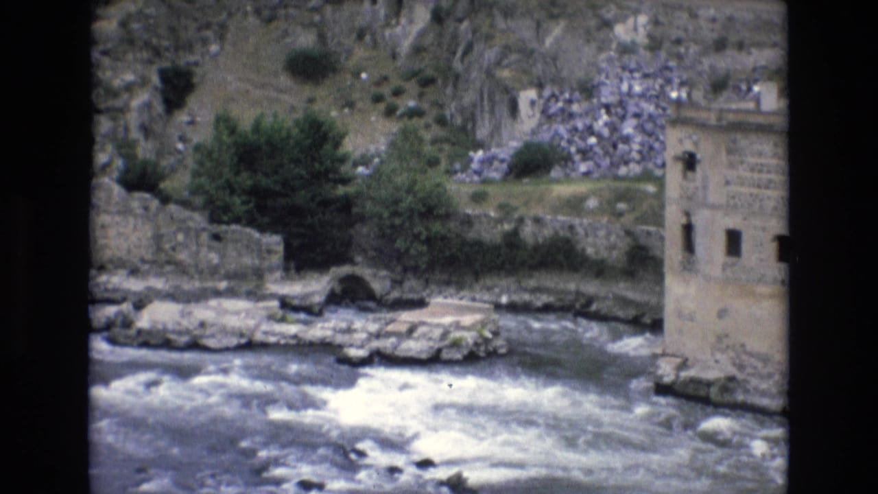 River beside stone walls and a tall masonry building.
