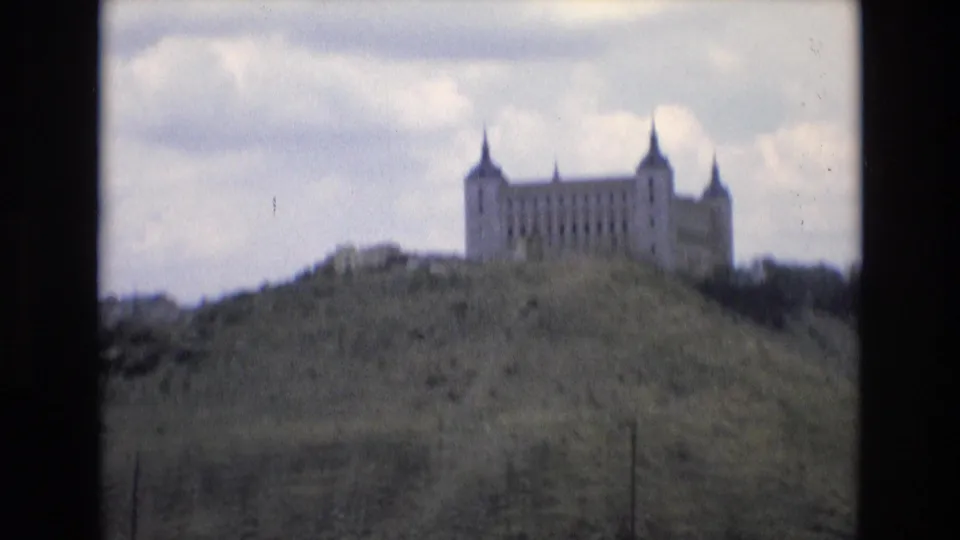 A distant fortified-looking landmark stands along a Spanish hillside in this 1972 8mm travel frame, with clouds and muted green terrain visible.