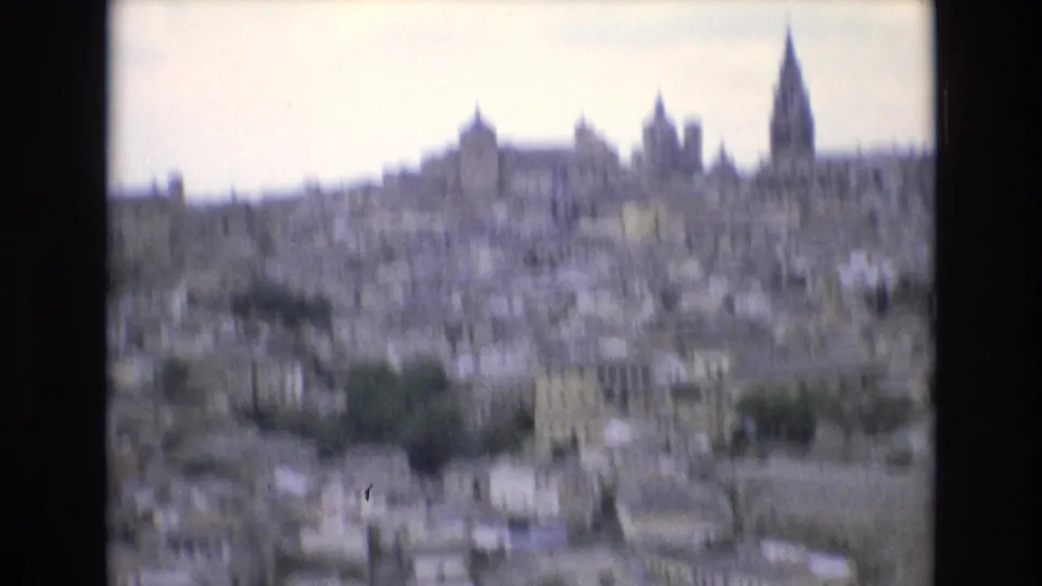 1972 Spain 8mm frame showing an overexposed, soft-focus city panorama with a tall spire, church towers, pale buildings, and a high overlook perspective.
