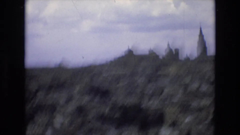 Soft 8mm frame from Spain showing rocky hillside foreground and a distant historic skyline with towers and a tall spire.