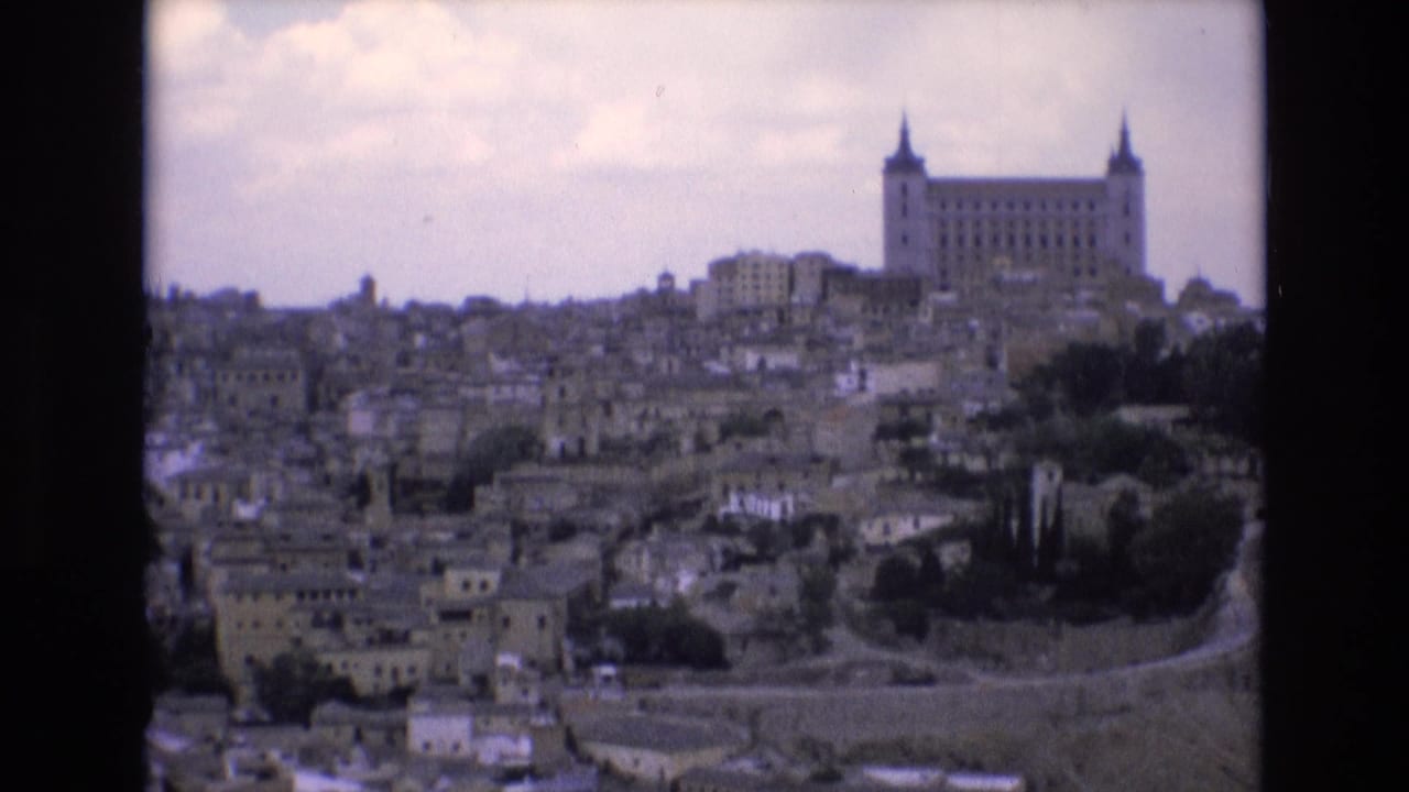 1972 8mm travel frame showing Toledo, Spain, with the Alcazar rising above dense stone buildings on a hill under a cloudy sky.