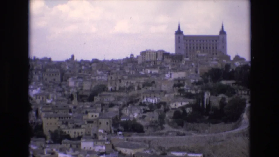 1972 8mm travel frame showing Toledo, Spain, with the Alcazar rising above dense stone buildings on a hill under a cloudy sky.