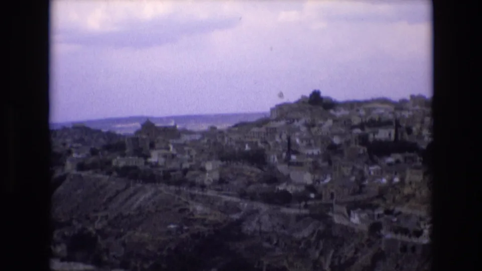 Later frame in the 1972 Toledo panorama, with clustered hillside buildings, terraced slopes, a distant horizon, and dark 8mm frame edges.