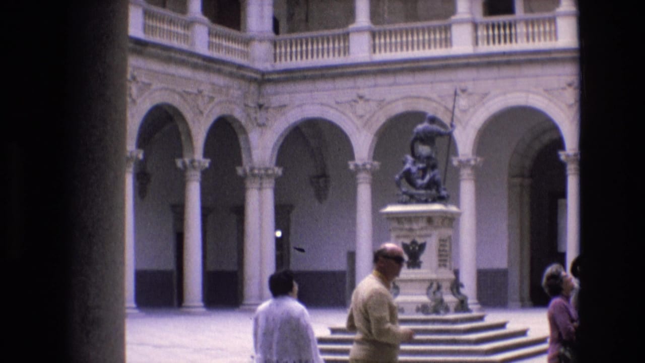 Several visitors walk across a courtyard toward a central statue and steps.
