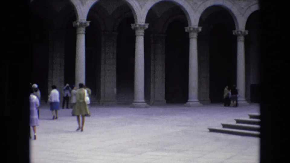 1972 Spain frame with visitors scattered across a historic courtyard, including people walking, pausing, and looking toward the surrounding stone arcade.