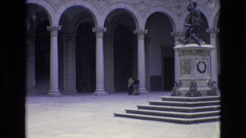1972 Spain travel frame with a stone monument and statue in a colonnaded courtyard, with two distant people standing near the base.