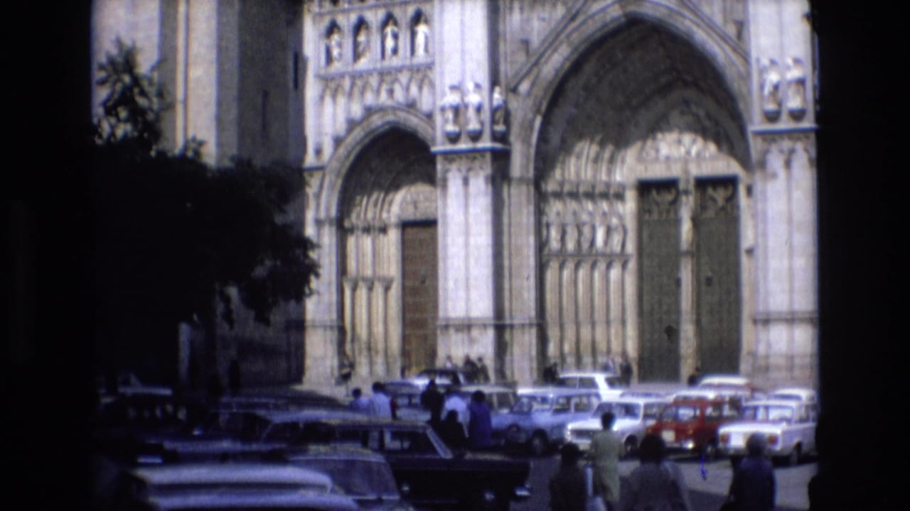Large cathedral doors with cars and small groups of people in front.