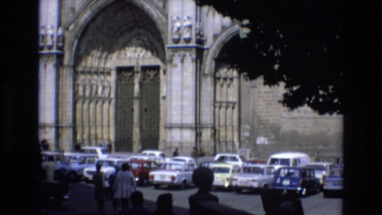 Cathedral doors and arched stonework overlook a crowded lot of parked cars and pedestrians.