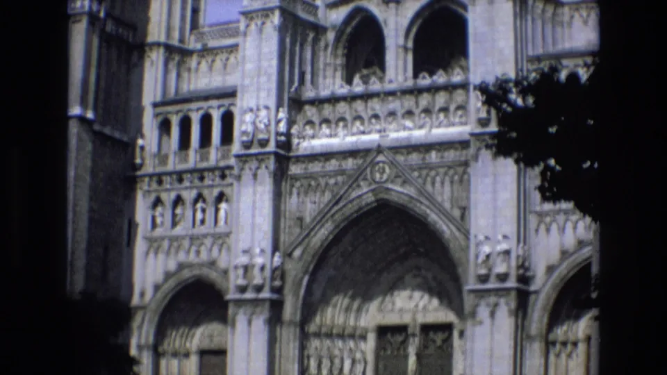 1972 Spain home-movie frame with a closer, upward-tilted view of the Gothic cathedral facade, showing arched openings, carved stonework, and the top of the entrance.