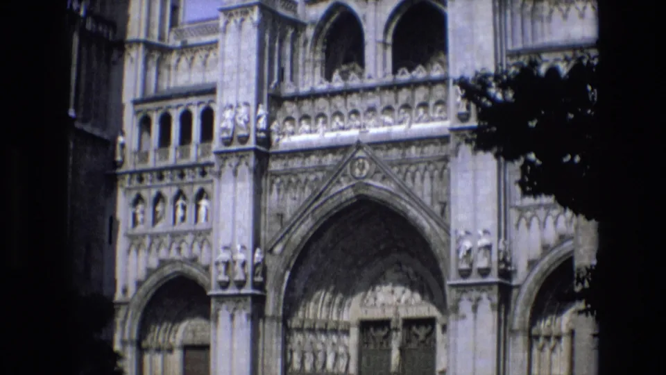 1972 Spain frame showing detailed Gothic cathedral stonework, arched openings, and a large recessed doorway, partly bordered by dark foliage or frame shadow.