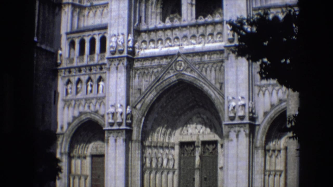 Spain 1972 home-movie frame showing a Gothic cathedral exterior with pointed arches, carved stone ornament, and tree shadow across the facade.