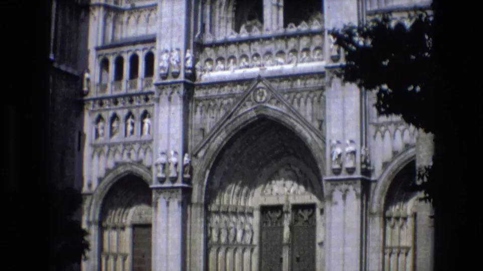 Spain 1972 home-movie frame showing a Gothic cathedral exterior with pointed arches, carved stone ornament, and tree shadow across the facade.