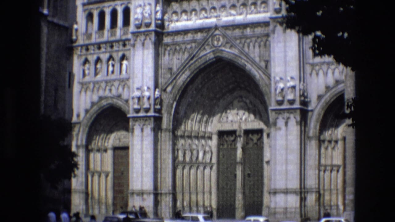 Cathedral facade with arched portals and parked cars along the curb.