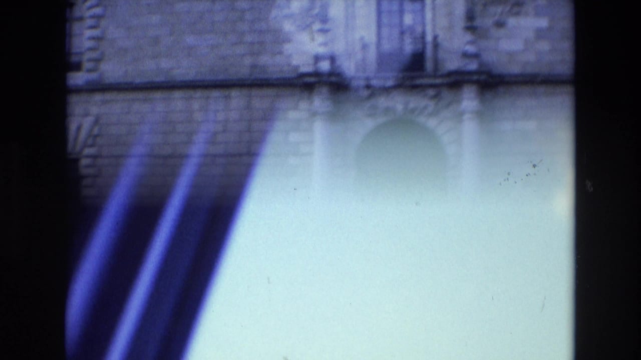 Opening 8mm frame from the Spain 1972 clip shows a partial building facade with strong light flare and blue color shift before the roadside scene appears.
