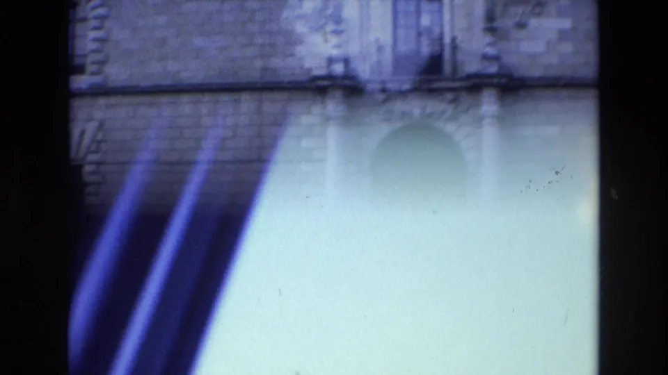 Opening 8mm frame from the Spain 1972 clip shows a partial building facade with strong light flare and blue color shift before the roadside scene appears.