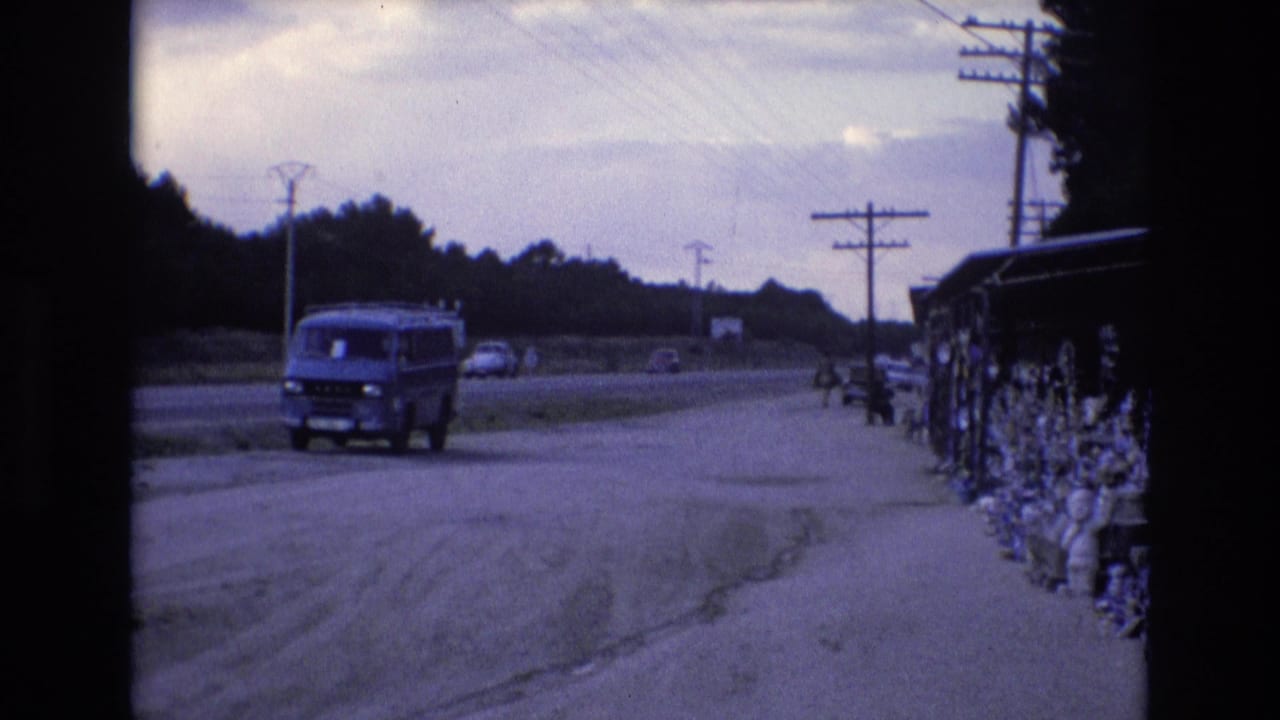 Blue van by the roadway with distant cars and a roadside display along the right edge.
