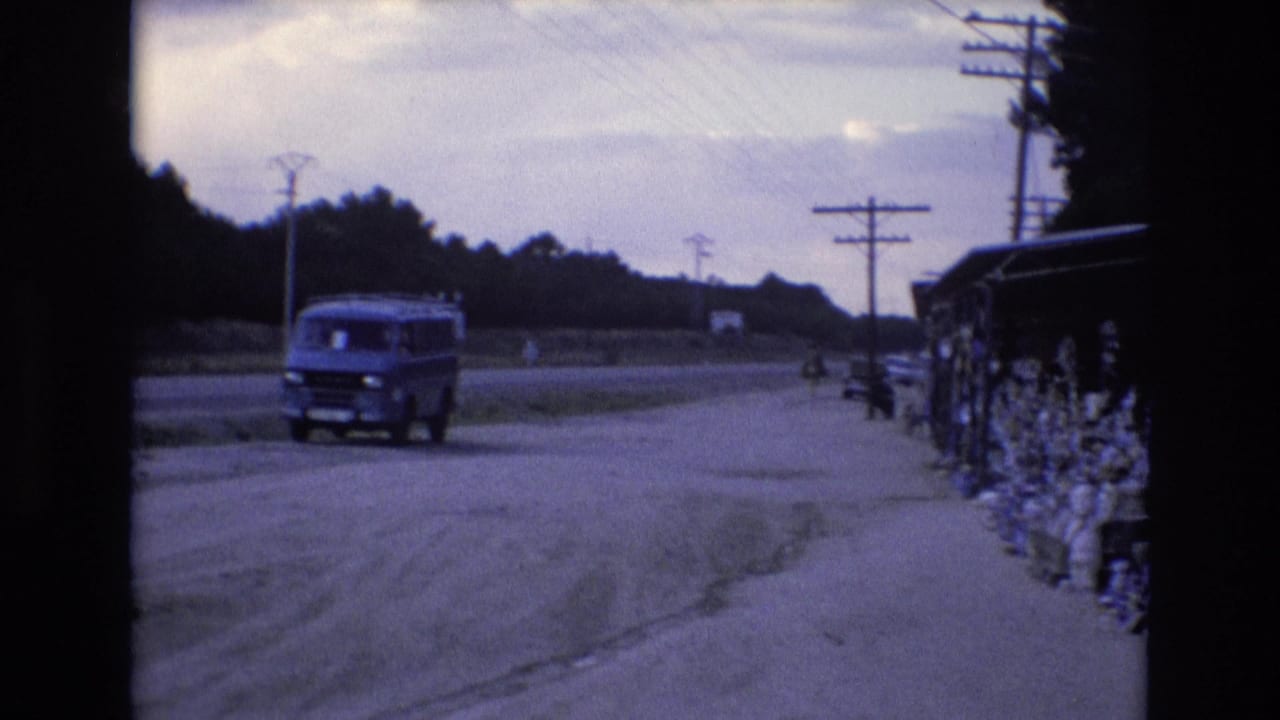Blue van passes a roadside area near a pottery stall and utility poles.