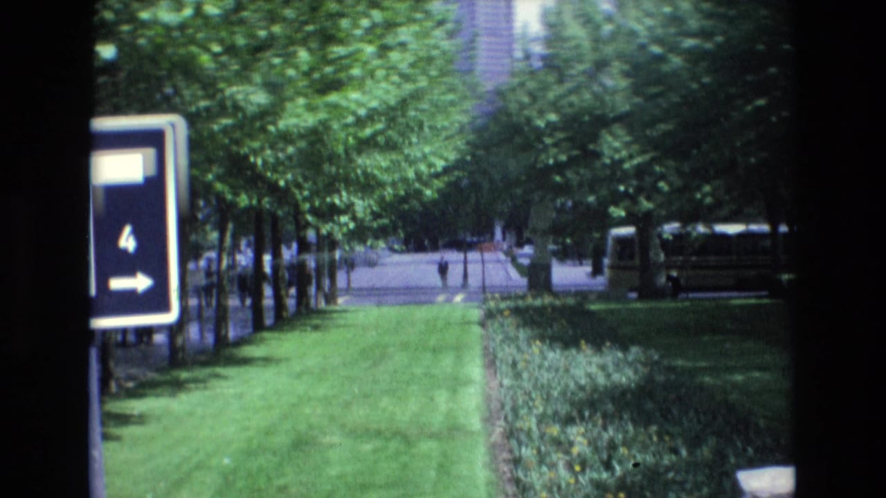 Grassy median with trees, sign, bus, and distant pedestrians.