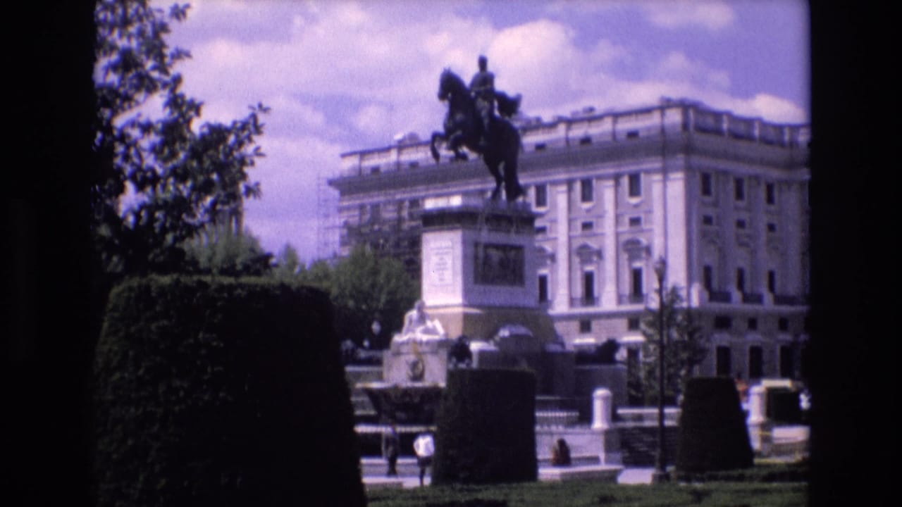 Equestrian statue in a formal park with clipped hedges, pedestrians, and a large pale building behind it.