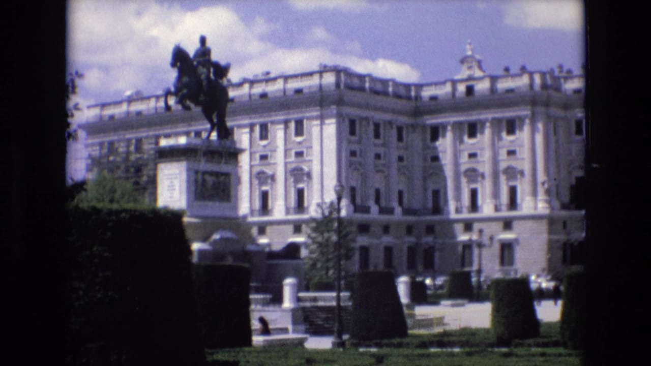 Palace exterior with equestrian statue, clipped hedges, garden paths, and bright clouded sky.
