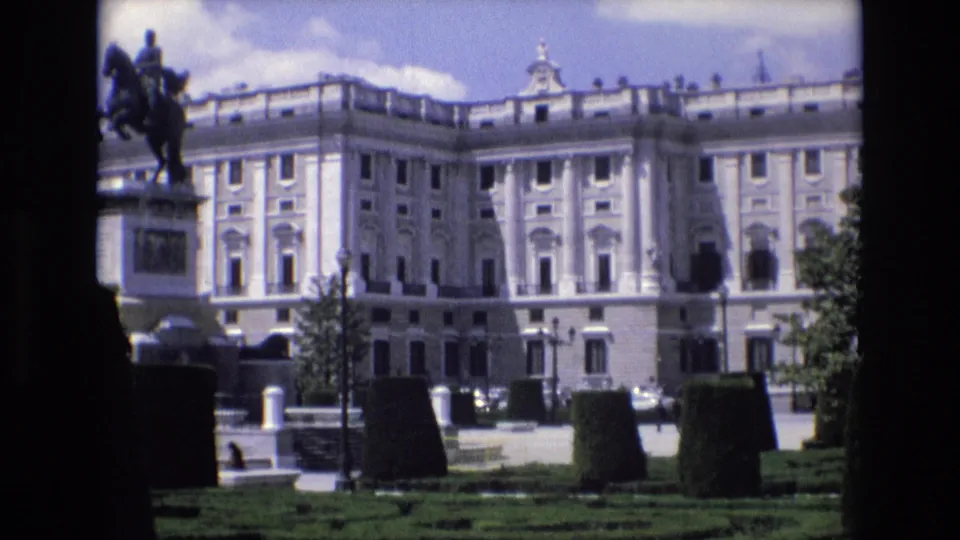 1972 Spain 8mm frame showing the palace facade and formal garden, with the equestrian statue partly cropped along the left edge and distant visitors near the paths.