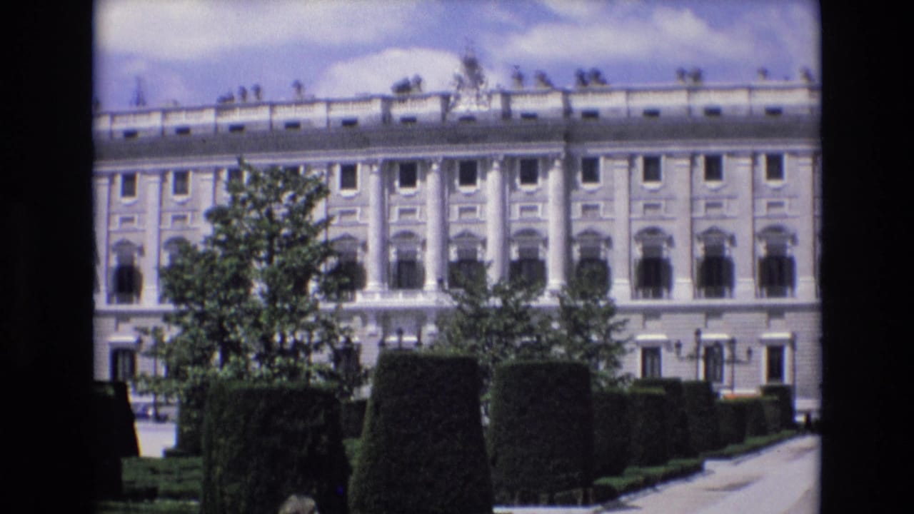 A large classical building in Spain, supported by the 1972 clip metadata, appears behind formal hedges and trees in a bright 8mm home-movie frame.