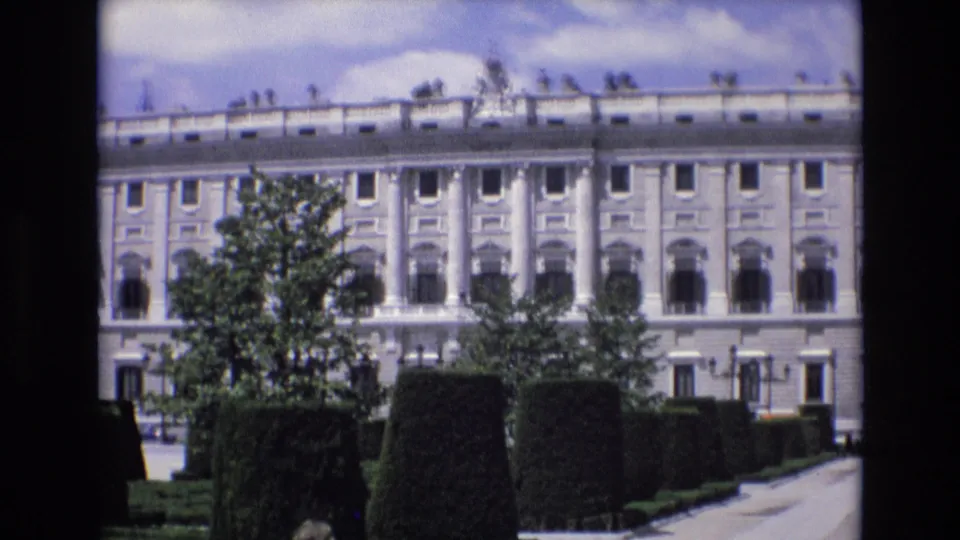 A large classical building in Spain, supported by the 1972 clip metadata, appears behind formal hedges and trees in a bright 8mm home-movie frame.